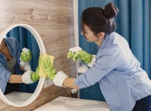 Housewife woking at home. Lady in a blue shirt. Woman clean mirror.